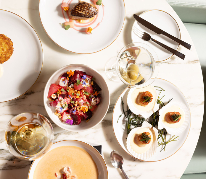 Elegant meal setup with grilled steak, asparagus, and side dishes on white plates with silverware, on a marble table.