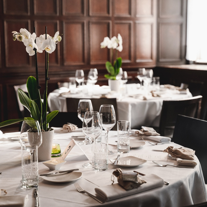 Elegant restaurant dining room with white orchid centerpieces on round tables set with wine glasses and brown napkins