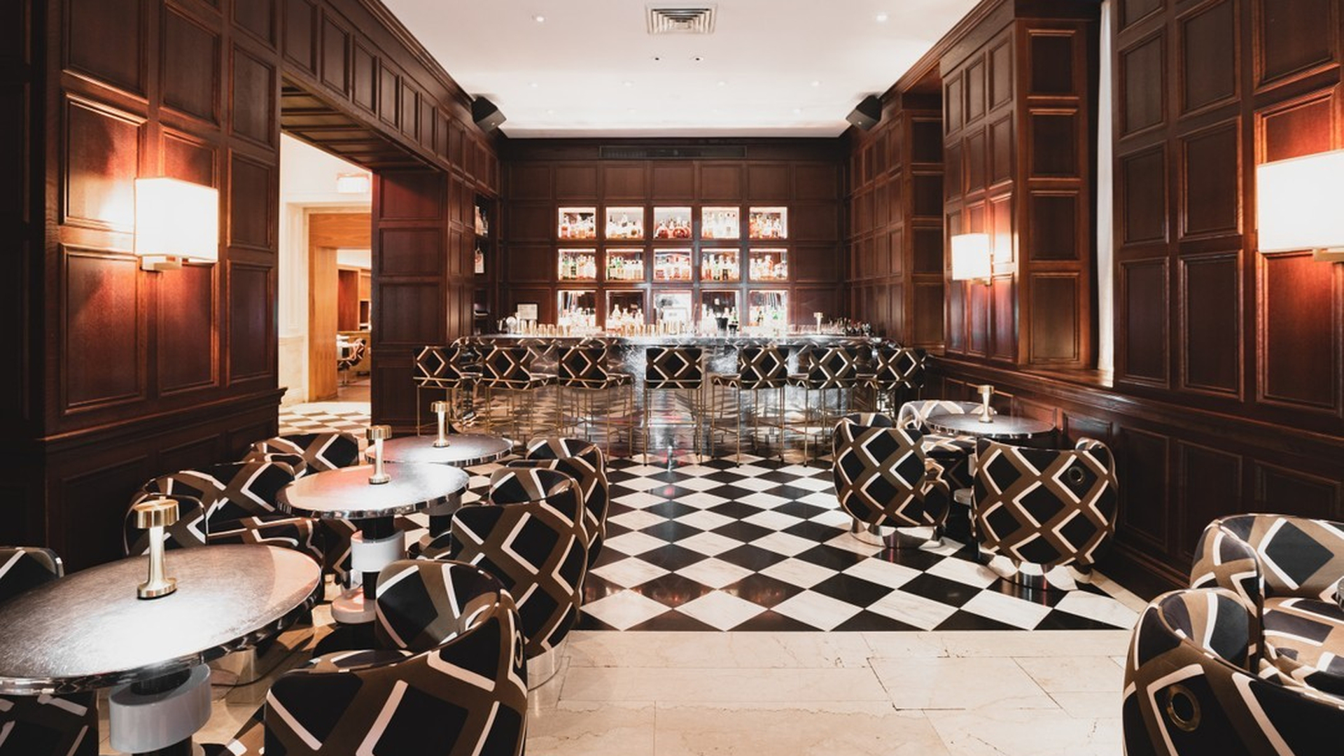 Cozy restaurant interior with green velvet chairs, marble tables, and wooden shelves filled with books.