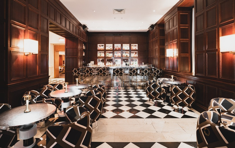 Restaurant interior with wooden shelves filled with books, tables with white tops and green booth seating.